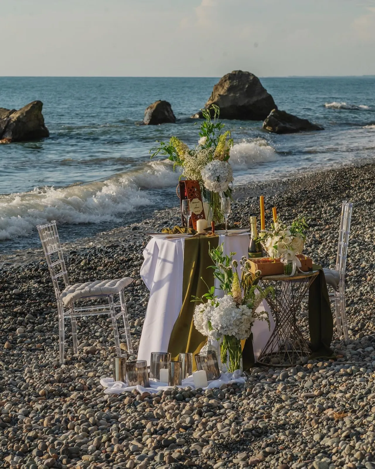 Table for two on a pebble beach by the sea rocks at golden hour