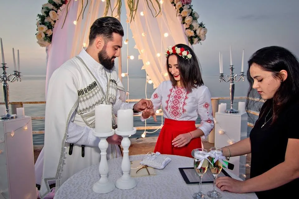Couple in a white chokha and an embroidered shirt lighting candles at a ceremony by the sea